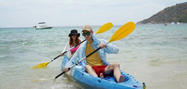 Genç çift, açık mavi bir kanoyla birlikte sarı raketlerle mutlu bir şekilde yol alıyorlar..