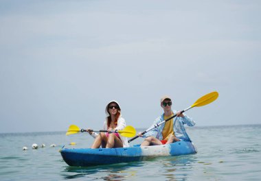 Genç çift, açık mavi bir kanoyla birlikte sarı raketlerle mutlu bir şekilde yol alıyorlar..