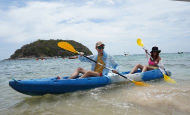 Genç çift, açık mavi bir kanoyla birlikte sarı raketlerle mutlu bir şekilde yol alıyorlar..