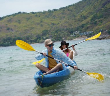Genç çift, açık mavi bir kanoyla birlikte sarı raketlerle mutlu bir şekilde yol alıyorlar..