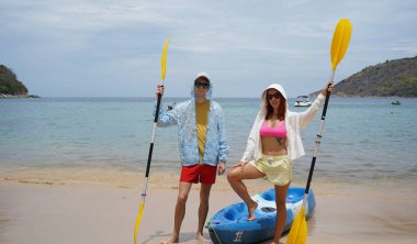 Kumsalda genç bir çift ellerinde kano kürekleri ve suda eğlenceli bir yolculuğa hazırlar..