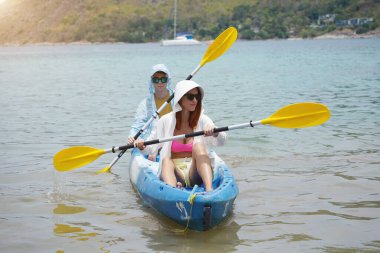 Genç çift, açık mavi bir kanoyla birlikte sarı raketlerle mutlu bir şekilde yol alıyorlar..