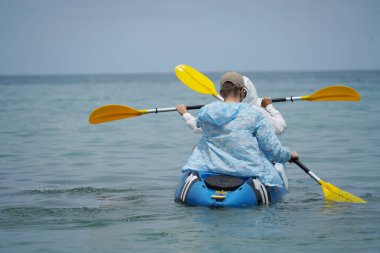 Genç çift, açık mavi bir kanoyla birlikte sarı raketlerle mutlu bir şekilde yol alıyorlar..