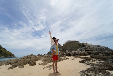 Genç bir çift kumsalda boş boş yürüyor, el ele tutuşuyor ve sıcak güneşin tadını çıkarıyor..