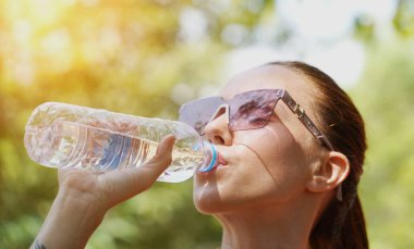 Bir adam ve bir kadın parkta birlikte koştuktan sonra şişelerden ferahlatıcı su içiyorlar..