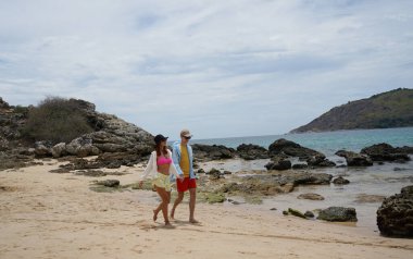 Genç bir çift kumsalda boş boş yürüyor, el ele tutuşuyor ve sıcak güneşin tadını çıkarıyor..