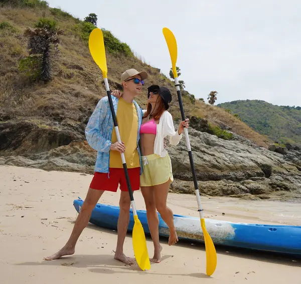 Kumsalda genç bir çift ellerinde kano kürekleri ve suda eğlenceli bir yolculuğa hazırlar..