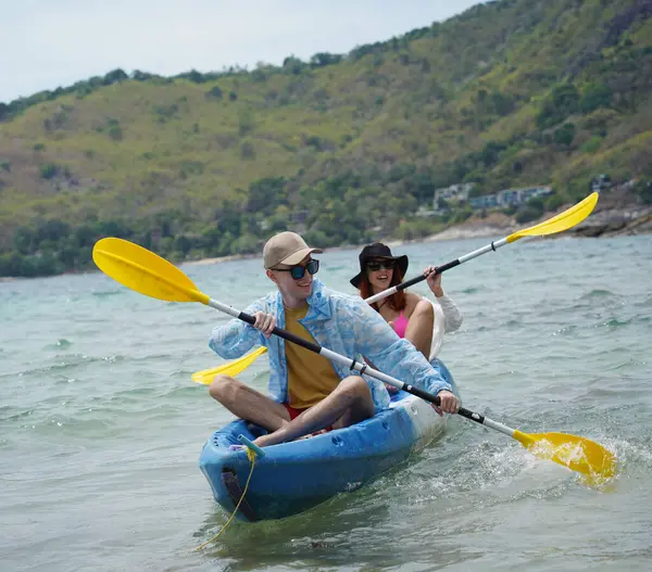 Genç çift, açık mavi bir kanoyla birlikte sarı raketlerle mutlu bir şekilde yol alıyorlar..