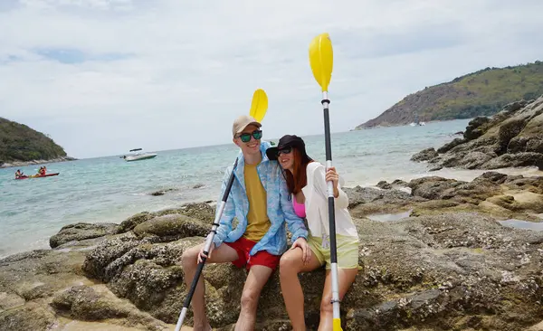 Kumsalda genç bir çift ellerinde kano kürekleri ve suda eğlenceli bir yolculuğa hazırlar..