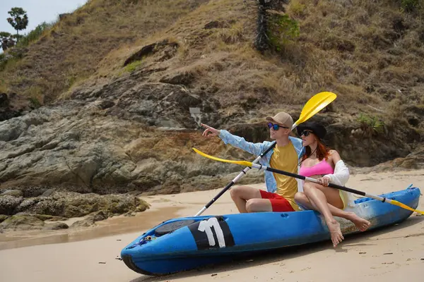 Kumsalda genç bir çift ellerinde kano kürekleri ve suda eğlenceli bir yolculuğa hazırlar..