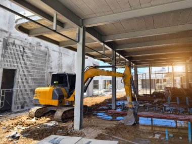 Sarı bir kazıcı inşaat halindeki bir binanın önünde..