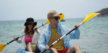 Genç çift, açık mavi bir kanoyla birlikte sarı raketlerle mutlu bir şekilde yol alıyorlar..