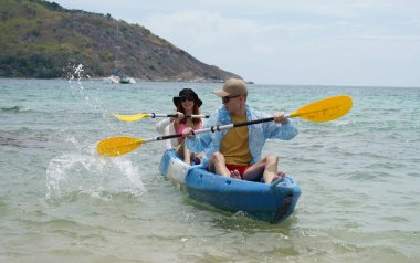 Genç çift, açık mavi bir kanoyla birlikte sarı raketlerle mutlu bir şekilde yol alıyorlar..