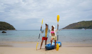 Kumsalda genç bir çift ellerinde kano kürekleri ve suda eğlenceli bir yolculuğa hazırlar..