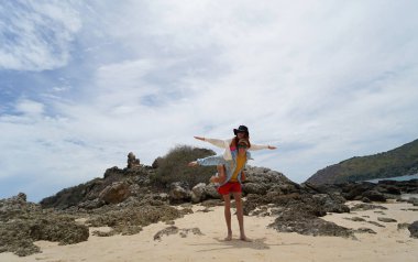 Genç bir çift kumsalda boş boş yürüyor, el ele tutuşuyor ve sıcak güneşin tadını çıkarıyor..