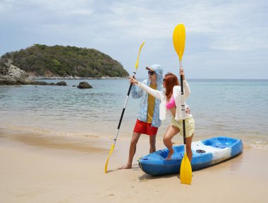 Kumsalda genç bir çift ellerinde kano kürekleri ve suda eğlenceli bir yolculuğa hazırlar..