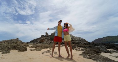 Genç bir çift kumsalda boş boş yürüyor, el ele tutuşuyor ve sıcak güneşin tadını çıkarıyor..