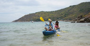 Genç çift, açık mavi bir kanoyla birlikte sarı raketlerle mutlu bir şekilde yol alıyorlar..