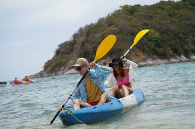 Genç çift, açık mavi bir kanoyla birlikte sarı raketlerle mutlu bir şekilde yol alıyorlar..