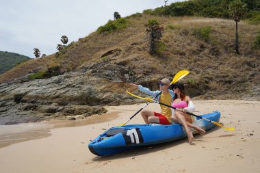 Kumsalda genç bir çift ellerinde kano kürekleri ve suda eğlenceli bir yolculuğa hazırlar..