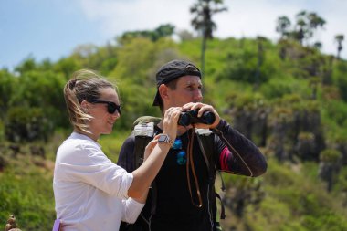 Bir erkek ve bir kadın dikkatle dürbünle uzaktan ilginç bir şeye bakıyorlar..