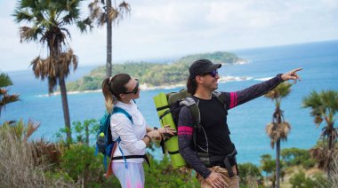 Genç bir çift okyanus manzarası sunan engebeli kayalık bir uçurumda yürüyüş yapıyor..