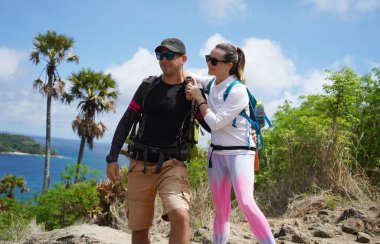 Genç bir çift okyanus manzarası sunan engebeli kayalık bir uçurumda yürüyüş yapıyor..