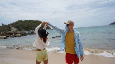 Genç bir çift kumsalda boş boş yürüyor, el ele tutuşuyor ve sıcak güneşin tadını çıkarıyor..