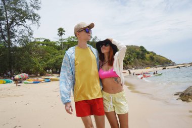 Genç bir çift kumsalda boş boş yürüyor, el ele tutuşuyor ve sıcak güneşin tadını çıkarıyor..