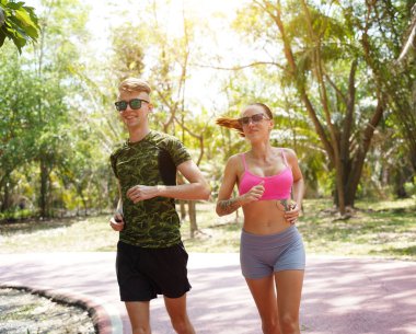 Bir adam ve bir kadın güzel bir parkta birlikte koşuyorlar, temiz havanın tadını çıkarıyorlar.