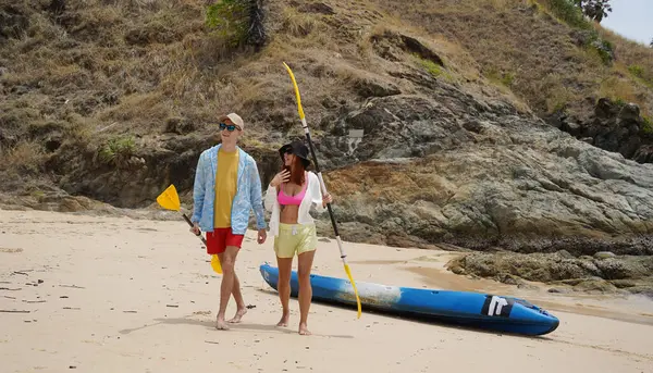 Kumsalda genç bir çift ellerinde kano kürekleri ve suda eğlenceli bir yolculuğa hazırlar..