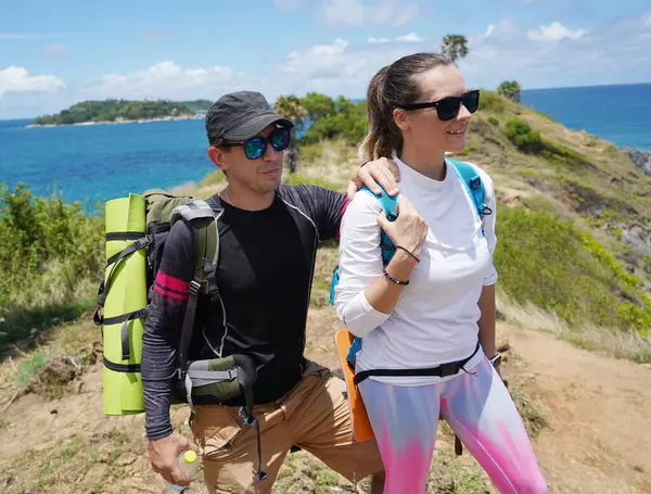 Genç bir çift okyanus manzarası sunan engebeli kayalık bir uçurumda yürüyüş yapıyor..