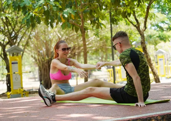 Renkli bir yoga minderinde bacaklarını açarken bir erkek bir kadına yardım ediyor..