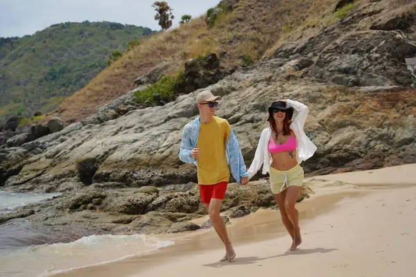 Genç bir çift kumsalda boş boş yürüyor, el ele tutuşuyor ve sıcak güneşin tadını çıkarıyor..