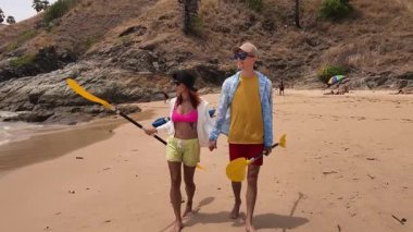 Genç bir çift kumsalda boş boş yürüyor, el ele tutuşuyor ve sıcak güneşin tadını çıkarıyor..