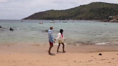 Genç bir çift kumsalda boş boş yürüyor, el ele tutuşuyor ve sıcak güneşin tadını çıkarıyor..