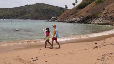 Genç bir çift kumsalda boş boş yürüyor, el ele tutuşuyor ve sıcak güneşin tadını çıkarıyor..