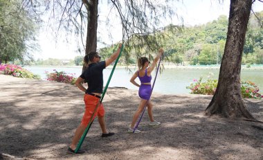 Genç çift parkta direniş bantlarıyla egzersiz yapıyor..