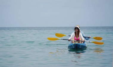 Genç çift, açık mavi bir kanoyla birlikte sarı raketlerle mutlu bir şekilde yol alıyorlar..