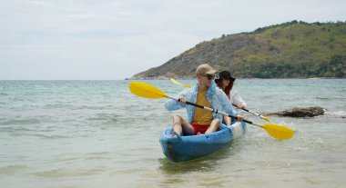 Genç çift, açık mavi bir kanoyla birlikte sarı raketlerle mutlu bir şekilde yol alıyorlar..