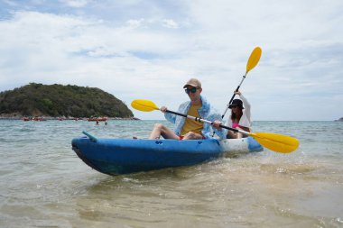 Genç çift, açık mavi bir kanoyla birlikte sarı raketlerle mutlu bir şekilde yol alıyorlar..