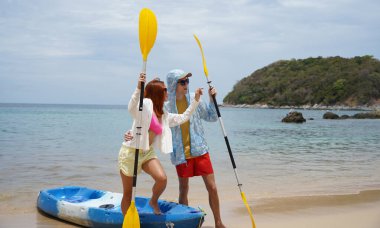 Kumsalda genç bir çift ellerinde kano kürekleri ve suda eğlenceli bir yolculuğa hazırlar..