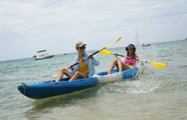 Genç çift, açık mavi bir kanoyla birlikte sarı raketlerle mutlu bir şekilde yol alıyorlar..
