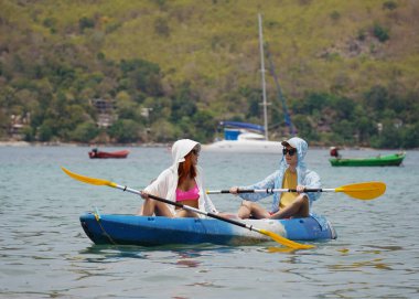 Genç çift, açık mavi bir kanoyla birlikte sarı raketlerle mutlu bir şekilde yol alıyorlar..