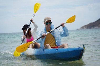 Genç çift, açık mavi bir kanoyla birlikte sarı raketlerle mutlu bir şekilde yol alıyorlar..