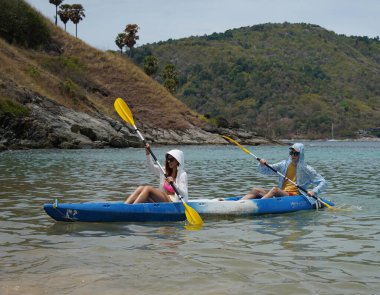 Genç çift, açık mavi bir kanoyla birlikte sarı raketlerle mutlu bir şekilde yol alıyorlar..