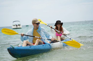Genç çift, açık mavi bir kanoyla birlikte sarı raketlerle mutlu bir şekilde yol alıyorlar..
