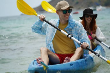 Genç çift, açık mavi bir kanoyla birlikte sarı raketlerle mutlu bir şekilde yol alıyorlar..