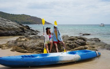 Kumsalda genç bir çift ellerinde kano kürekleri ve suda eğlenceli bir yolculuğa hazırlar..