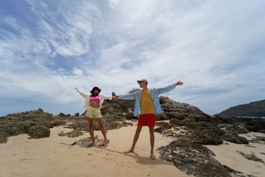 Genç bir çift kumsalda boş boş yürüyor, el ele tutuşuyor ve sıcak güneşin tadını çıkarıyor..